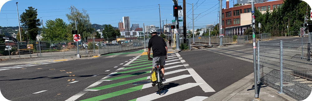 A person on a bike rides across a striped cross-bike green and white crosswalk